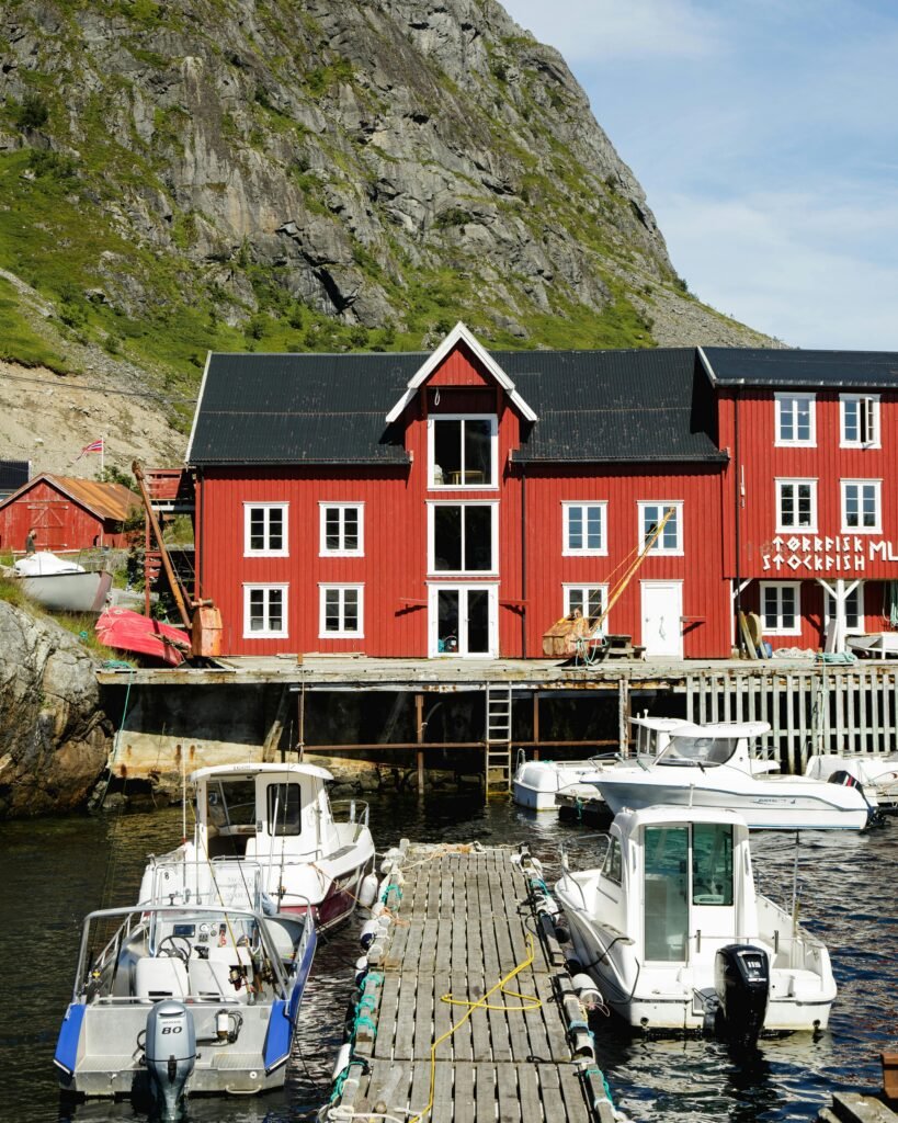 Red timber building in Å fishing village harbor with boats under clear sky.
