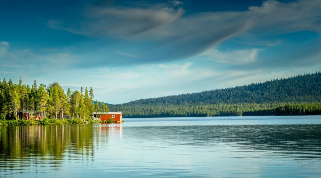 Idyllic Swedish lake scene with scenic red cabins and lush pine forest.