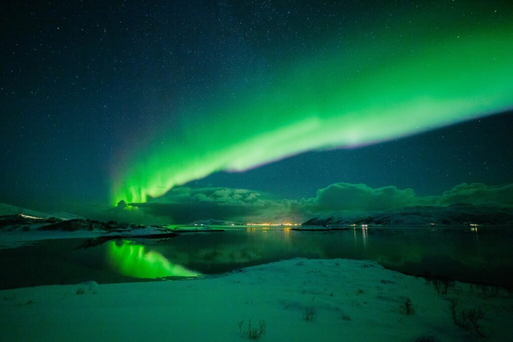 Stunning aurora borealis illuminating the night sky in Tromsø, Norway, reflecting on snowy landscape.