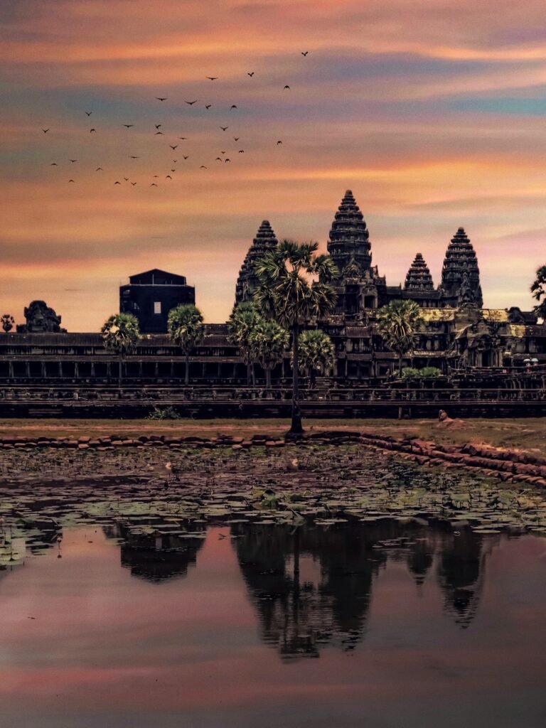 Majestic view of Angkor Wat at sunset with reflection in water, showcasing ancient architecture.
