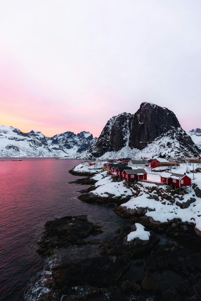 Picturesque snowy coastal village with red houses by the sea during a vibrant winter sunset.