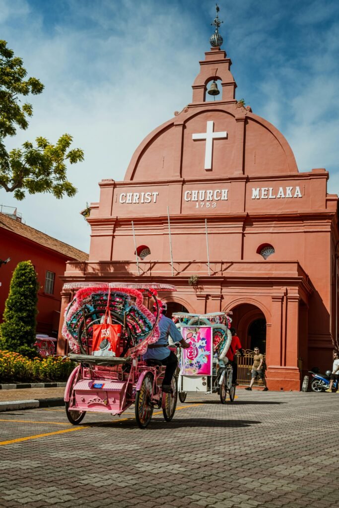 A vibrant view of trishaws in front of Christ Church in Malacca, Malaysia, under a bright sky.