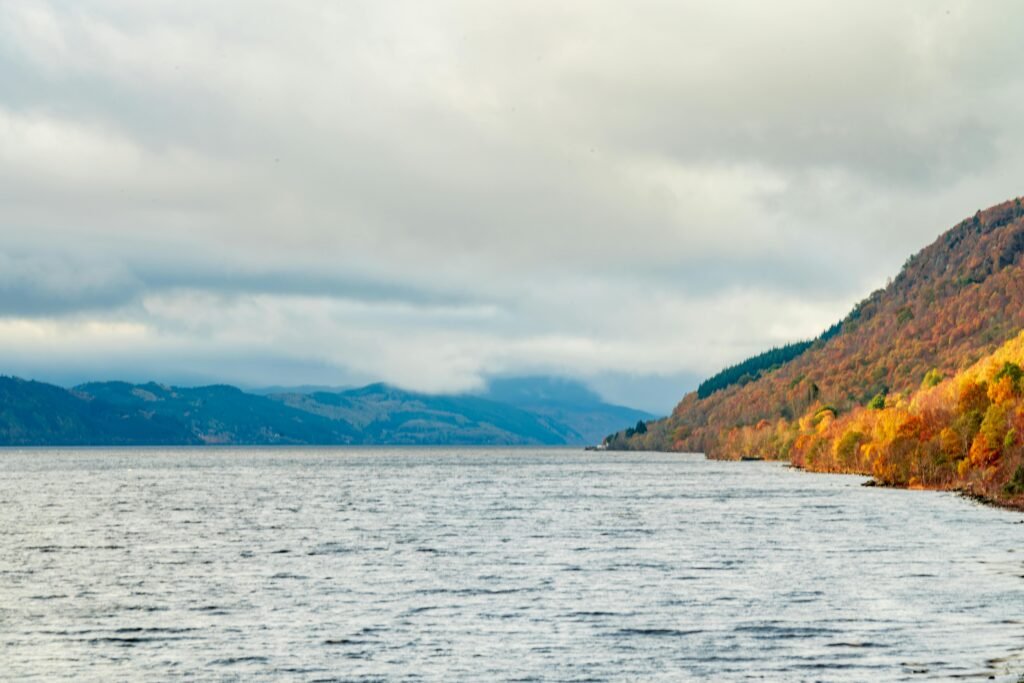 Scenic view of Loch Ness with autumn foliage and cloudy sky, perfectly capturing the essence of nature in fall.