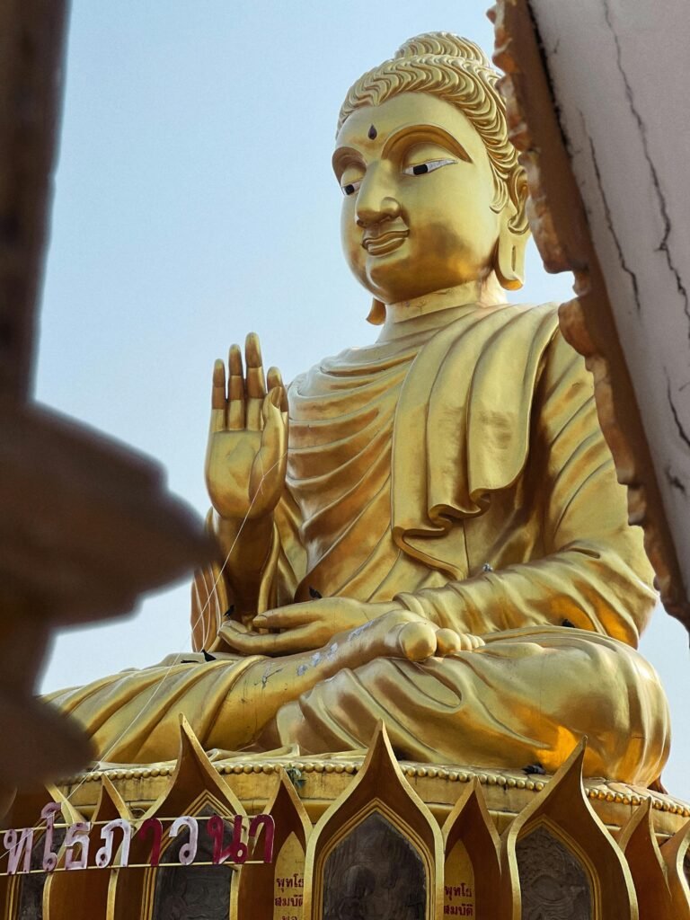 A majestic golden Buddha statue displayed prominently in a Thai temple, captured outdoors.