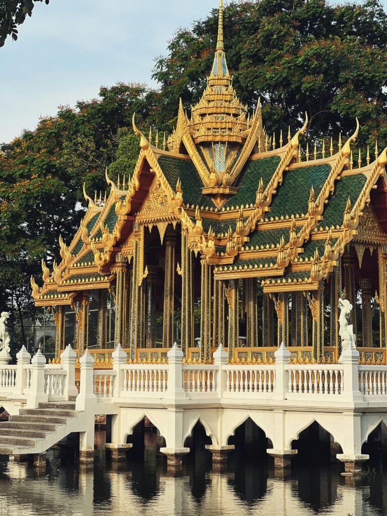 Beautiful Thai pavilion architecture with intricate details reflected in tranquil waters, surrounded by lush greenery.