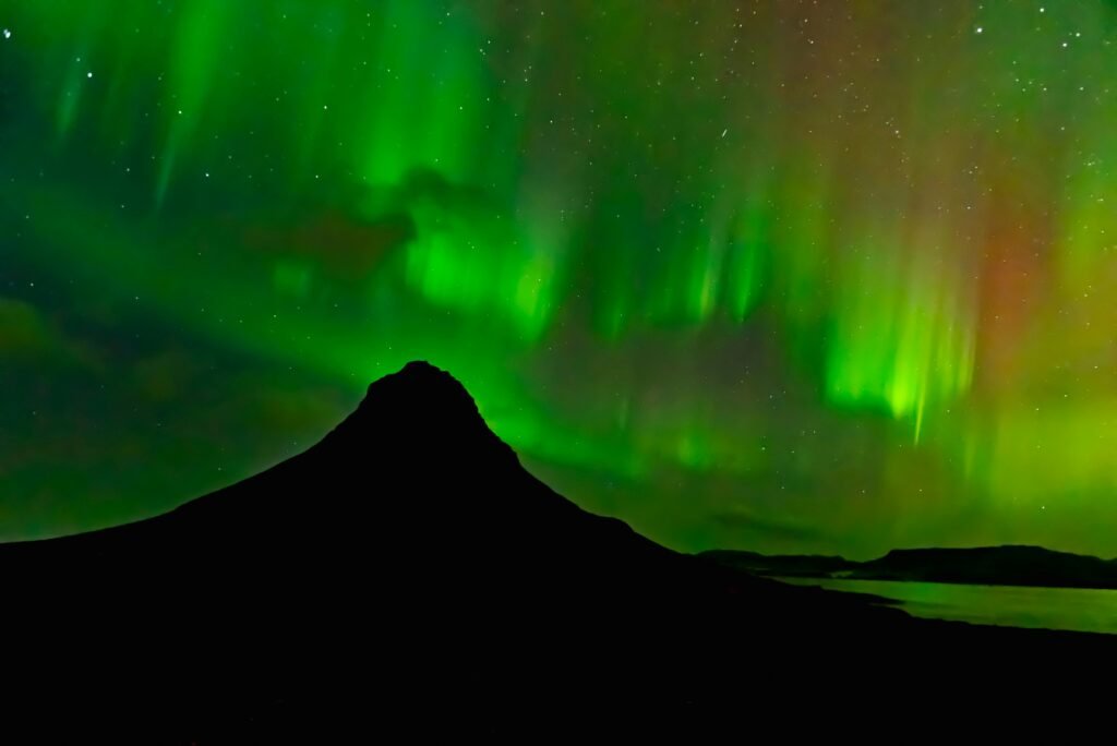 Stunning display of Northern Lights over Kirkjufell Mountain, Iceland, under starry night sky.