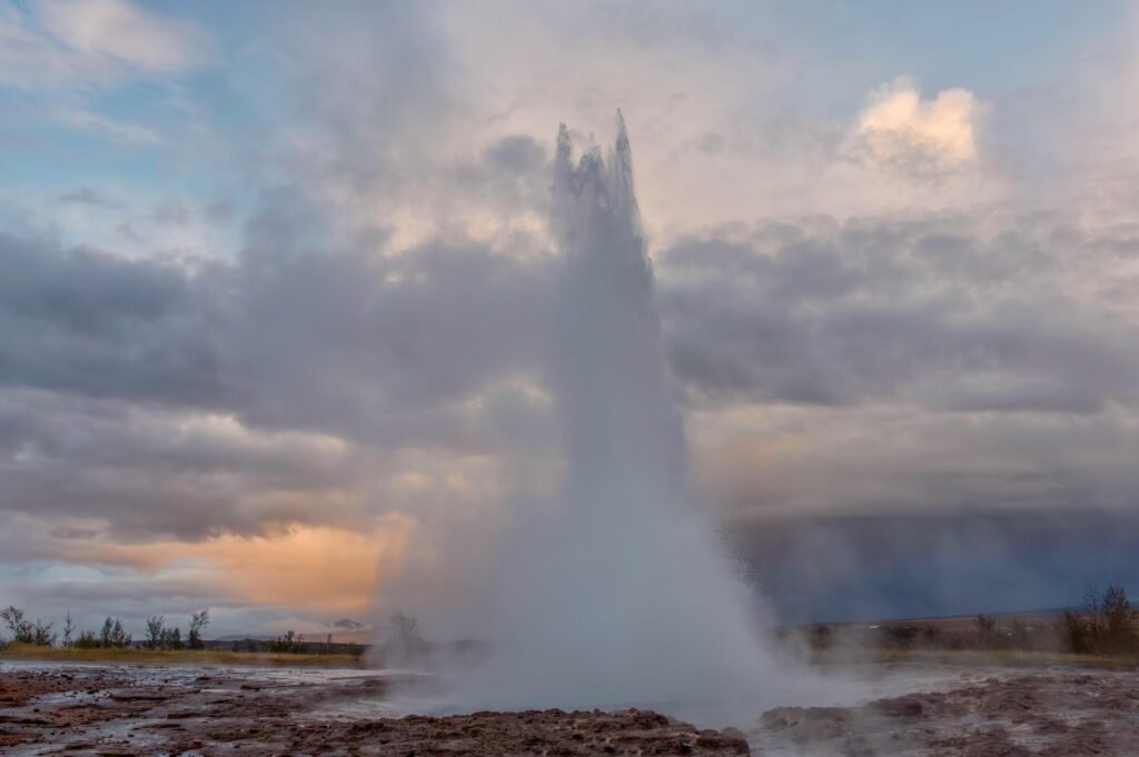 A dramatic eruption of the Strokkur geyser in Iceland against a vibrant evening sky.