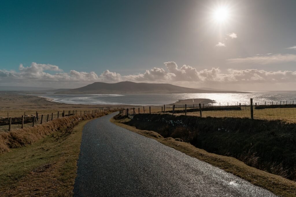 A picturesque coastal road in Ireland with rolling hills and ocean views under a bright sun.