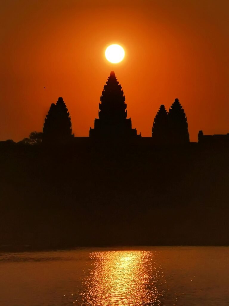 Majestic silhouette of Angkor Wat temple against a vibrant sunset with sun centered above the spire.
