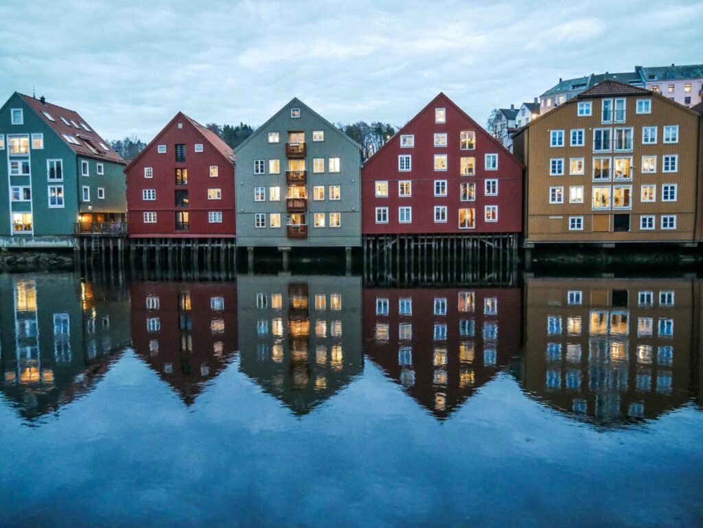 Contemporary residential building exteriors reflecting in water of lake under serene cloudy sky in town