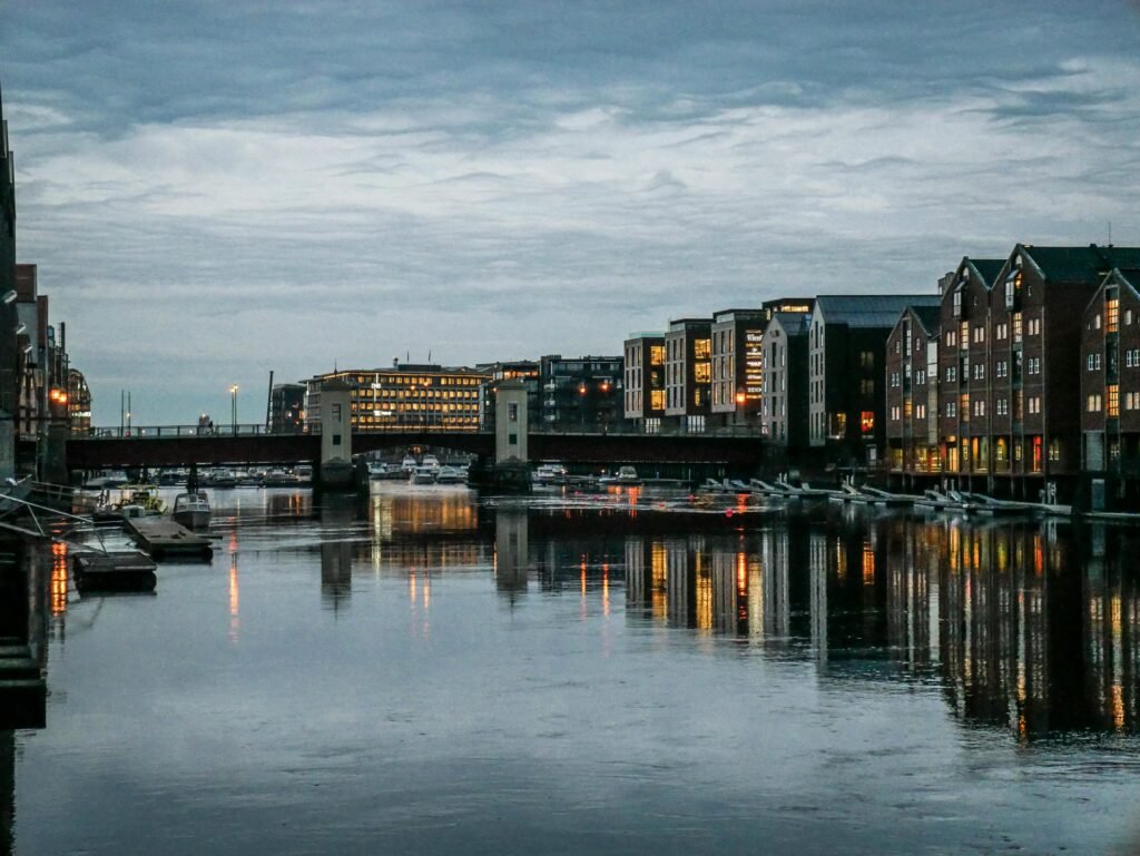Lake with rippled water reflecting contemporary residential house exteriors with shining lights under sky in evening