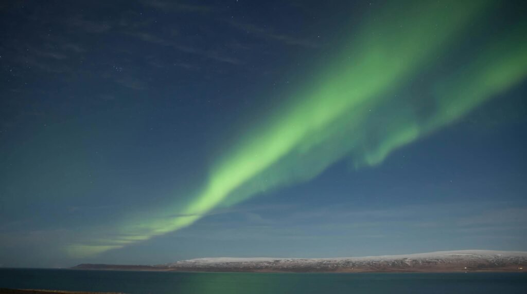 Vibrant aurora borealis above sea and snow in Búðardalur, Iceland.