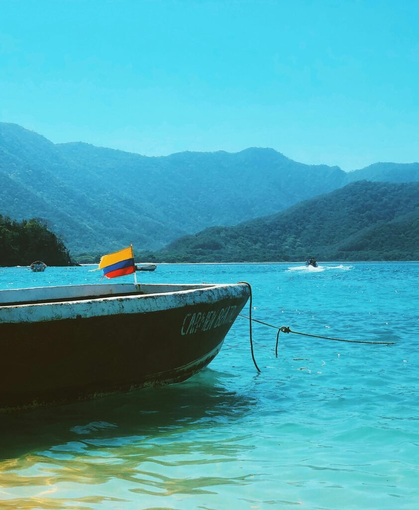 A boat with a flag floats on a turquoise sea against a mountainous backdrop.