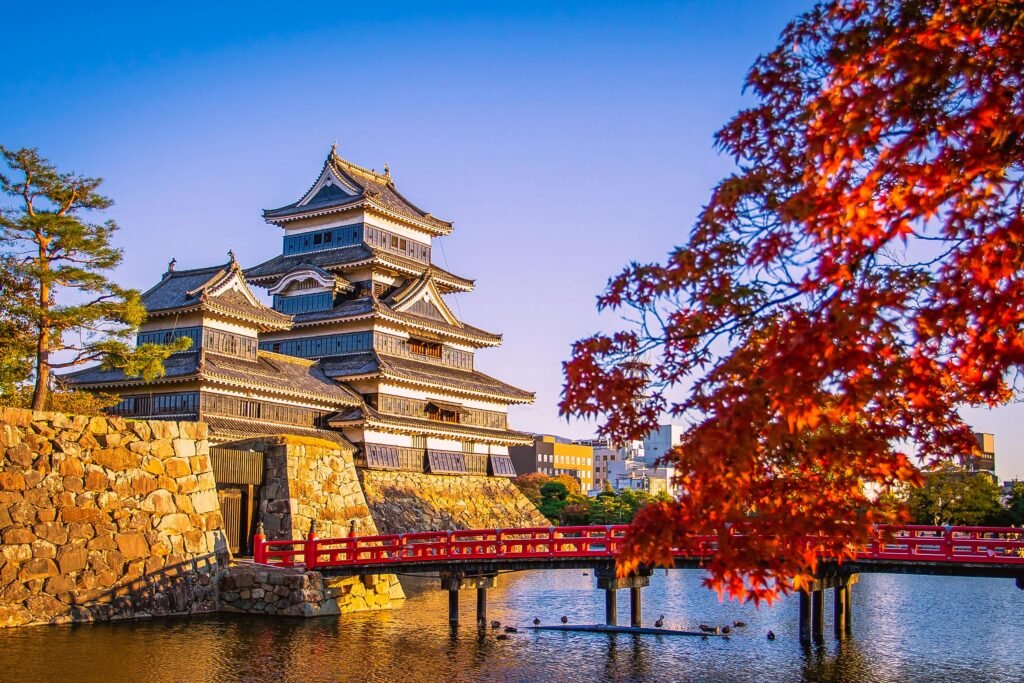 Scenic view of Matsumoto Castle with vibrant autumn foliage and a red bridge in Japan.