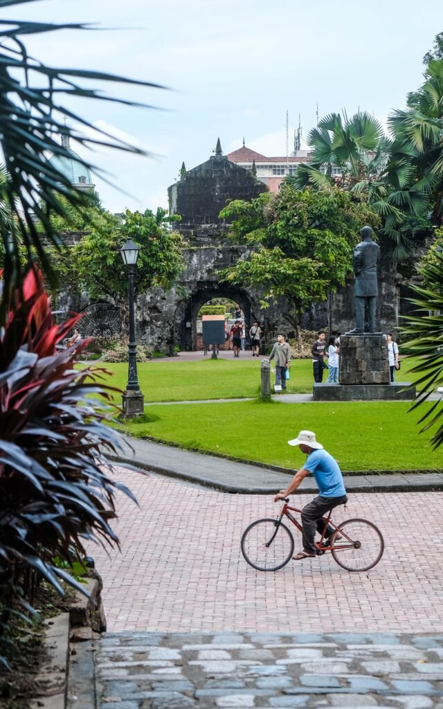 Cyclist in Intramuros, Manila with lush greenery and historical walls in view.