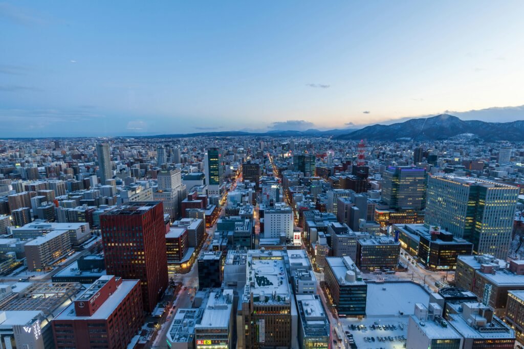 Captivating aerial view of Sapporo, Japan in winter at dusk with snow-covered buildings and distant mountains.