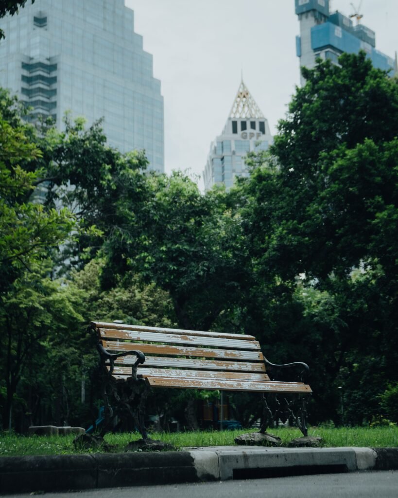 A quiet bench in Bangkok's Lumpini Park with a backdrop of skyscrapers and lush greenery.