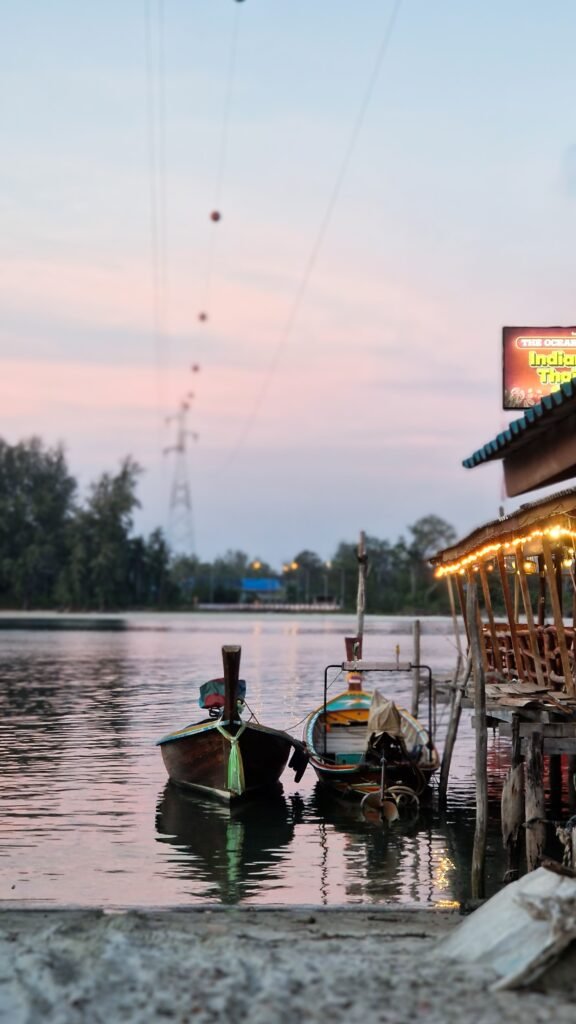 Tranquil view of traditional boats moored at sunset on a Thai river with colorful lights.
