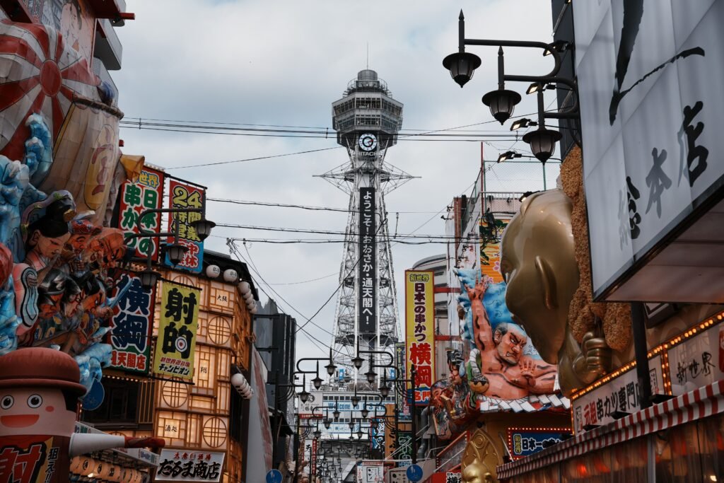 Vibrant street view of Osaka's Tsutenkaku Tower surrounded by colorful signs and architecture.